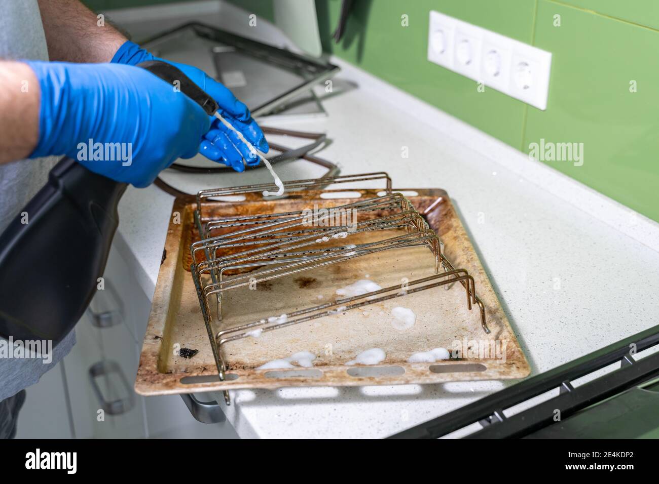 a man wearing blue rubber gloves cleans dirty grids and baking trays