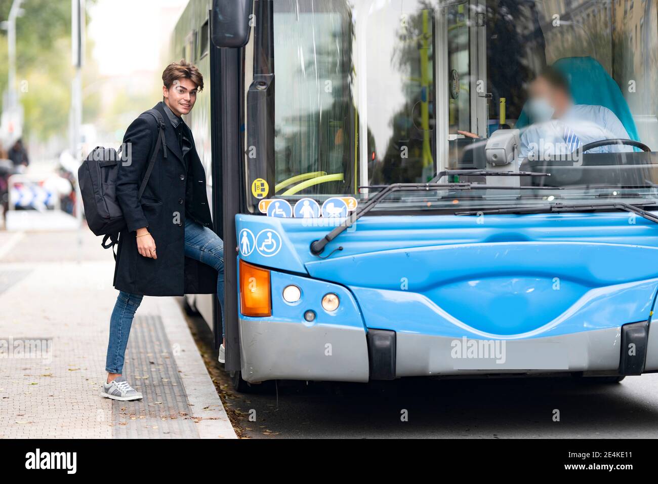 Smiling handsome young man with backpack boarding bus in city Stock Photo