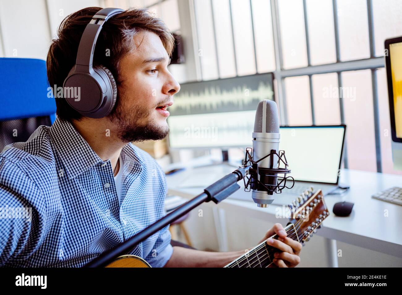 Male singer with headphones and microphone singing while playing guitar