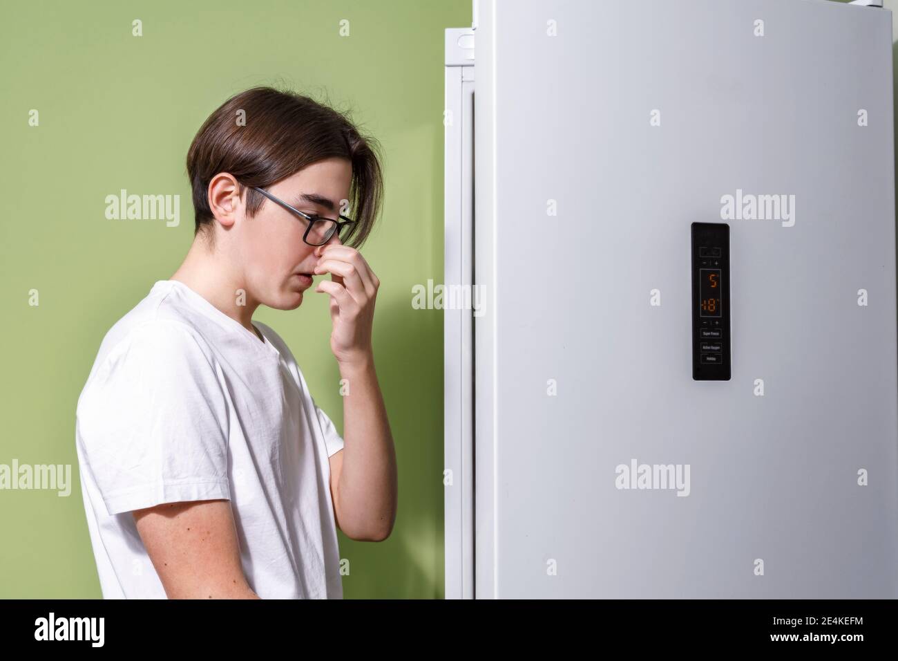 a young man in glasses and a white t-shirt smells unpleasant from his fridge Stock Photo