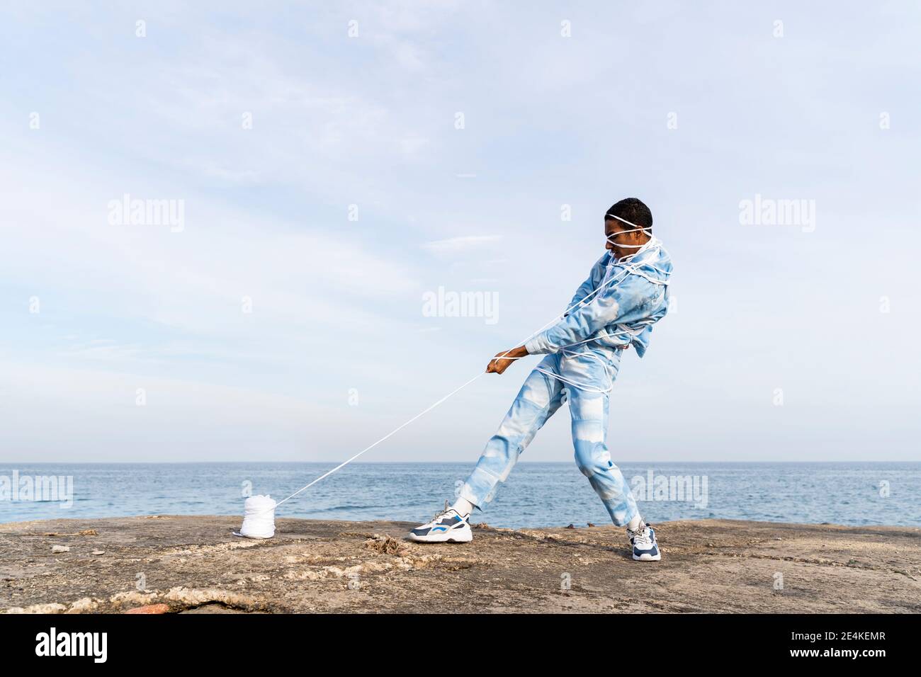Young man trying to set free from rope spool while standing against sky Stock Photo
