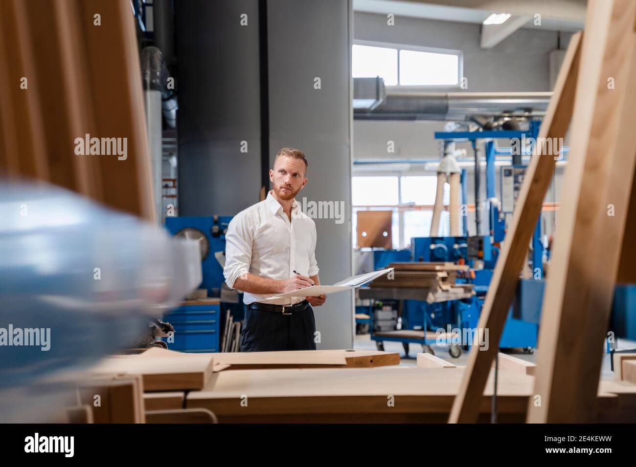 Carpenter standing in production hall with ring binder in hands Stock Photo
