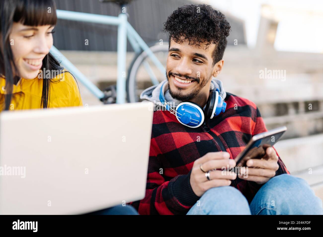 Smiling friends using laptop and digital tablet while sitting outdoors Stock Photo