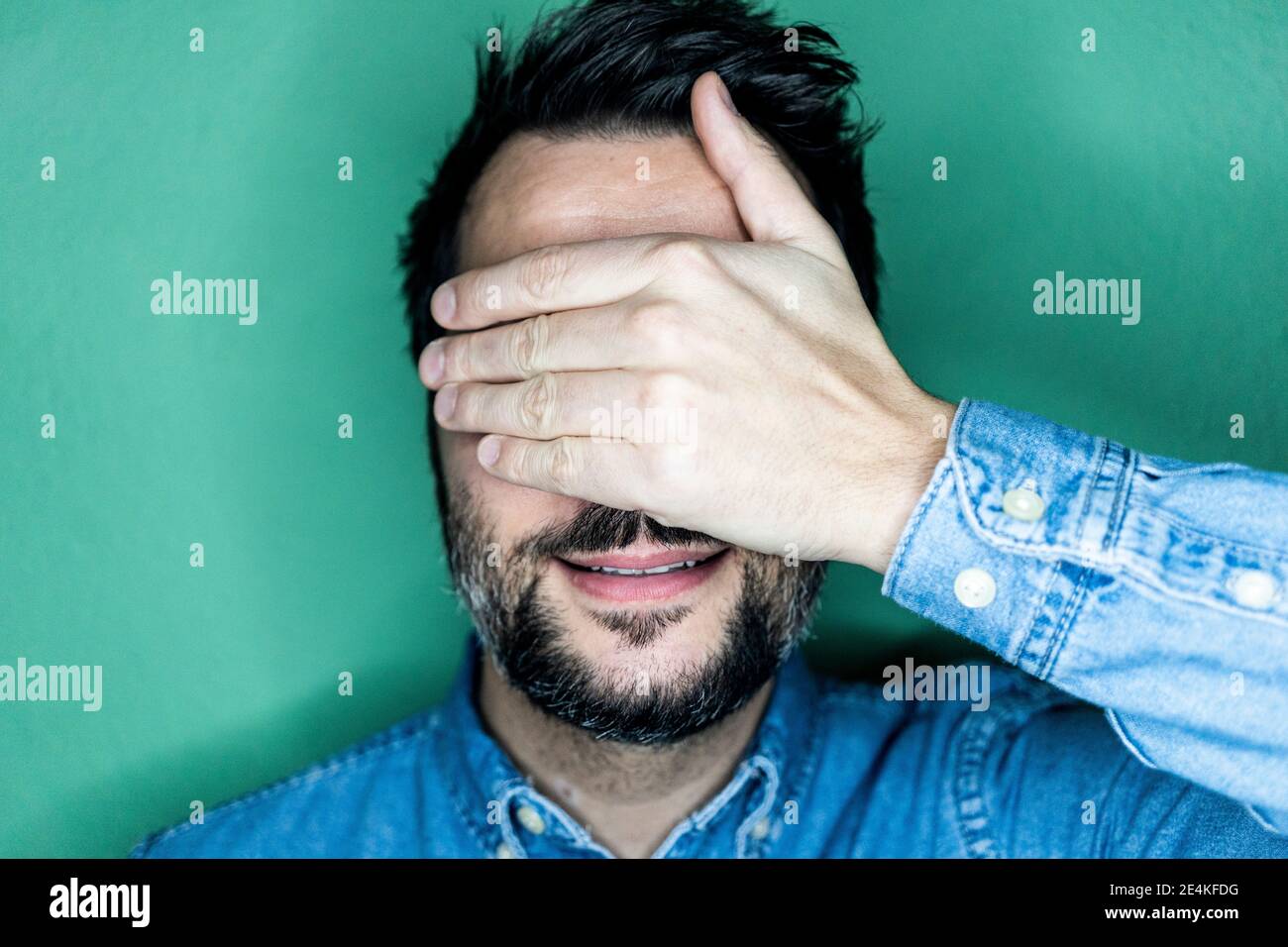 Studio portrait of smiling man covering eyes Stock Photo - Alamy
