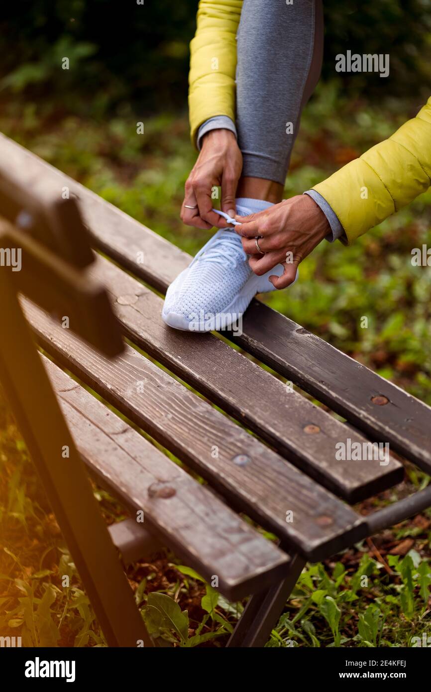 Sportswoman tying shoelace on bench while standing at park Stock Photo