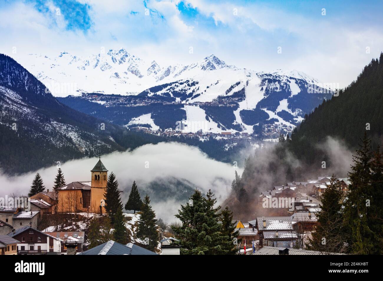 Champagny-en-Vanoise village panorama with mist and clouds around old church, over Courchevel resort on background Stock Photo