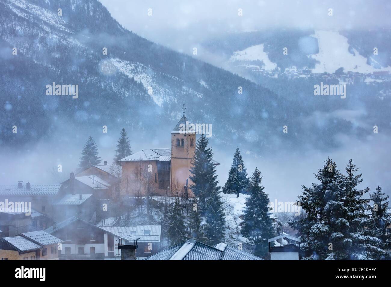 Church in Champagny-en-Vanoise village in France and view on Courchevel during heavy snowfall at winter Stock Photo