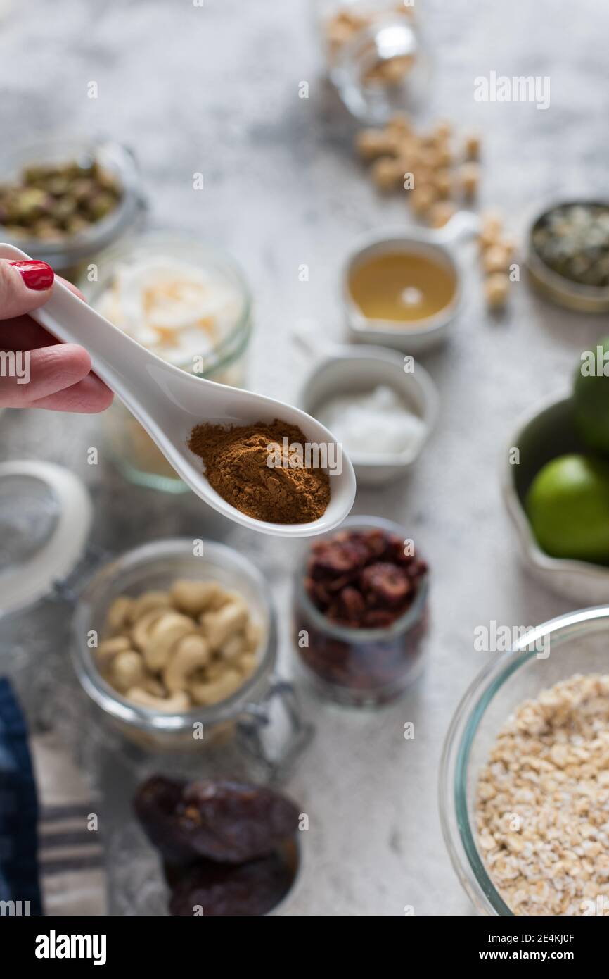 Woman hand holding a ceramic spoon full of ground cinnamon over some blurred granola ingredients. Stock Photo
