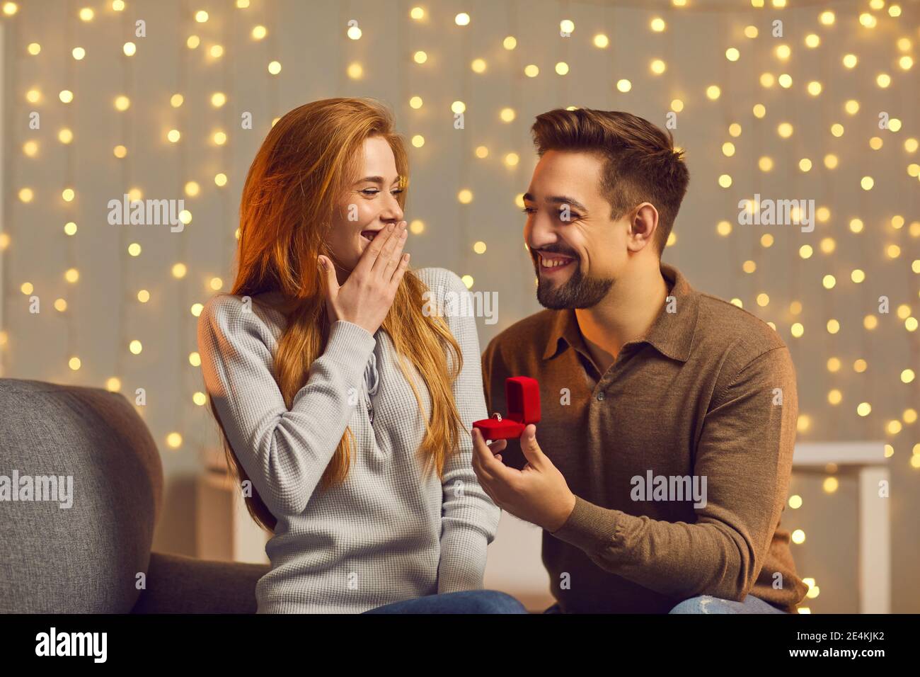 Happy young man making wonderful surprise for his girlfriend, giving her beautiful ring Stock Photo