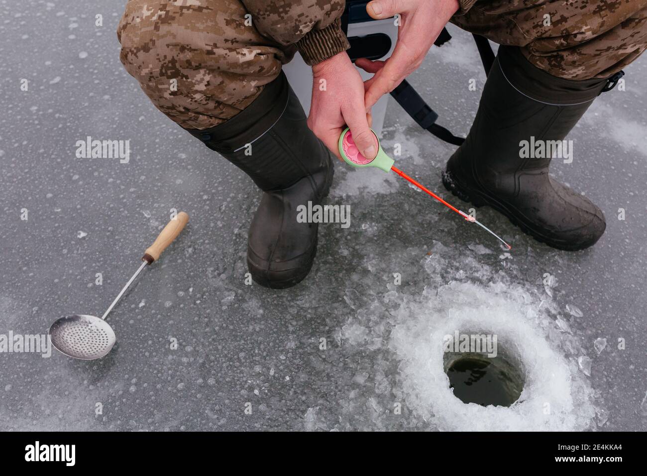 Faceless fisherman jiggling bait in an ice hole. Winter fishing on ice. Ice fishing. Man catching fish from ice  Stock Photo