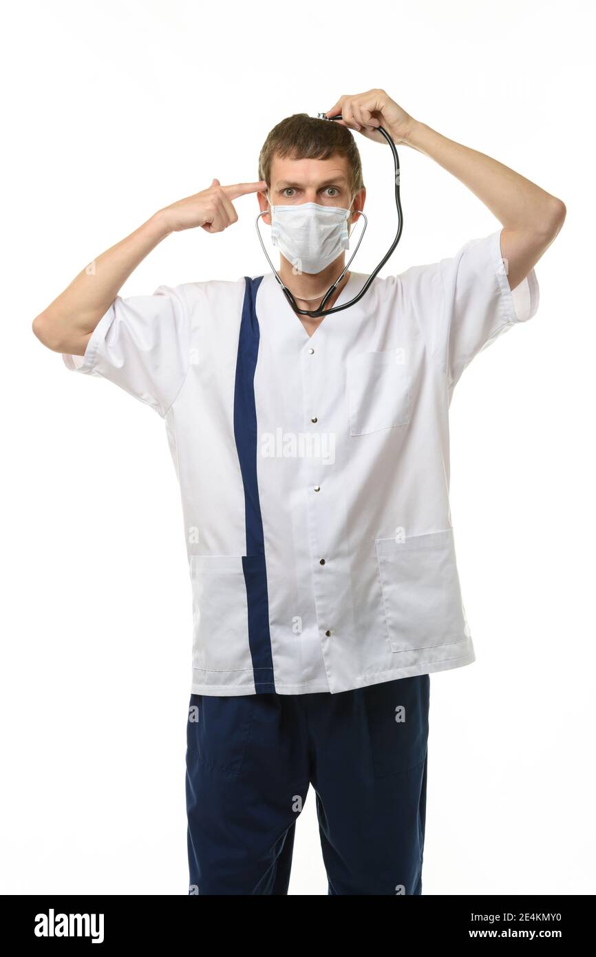 A masked doctor with a phonendoscope listens to his head, with the other hand he applied an impromptu pistol to his temple, isolated on a white backgr Stock Photo