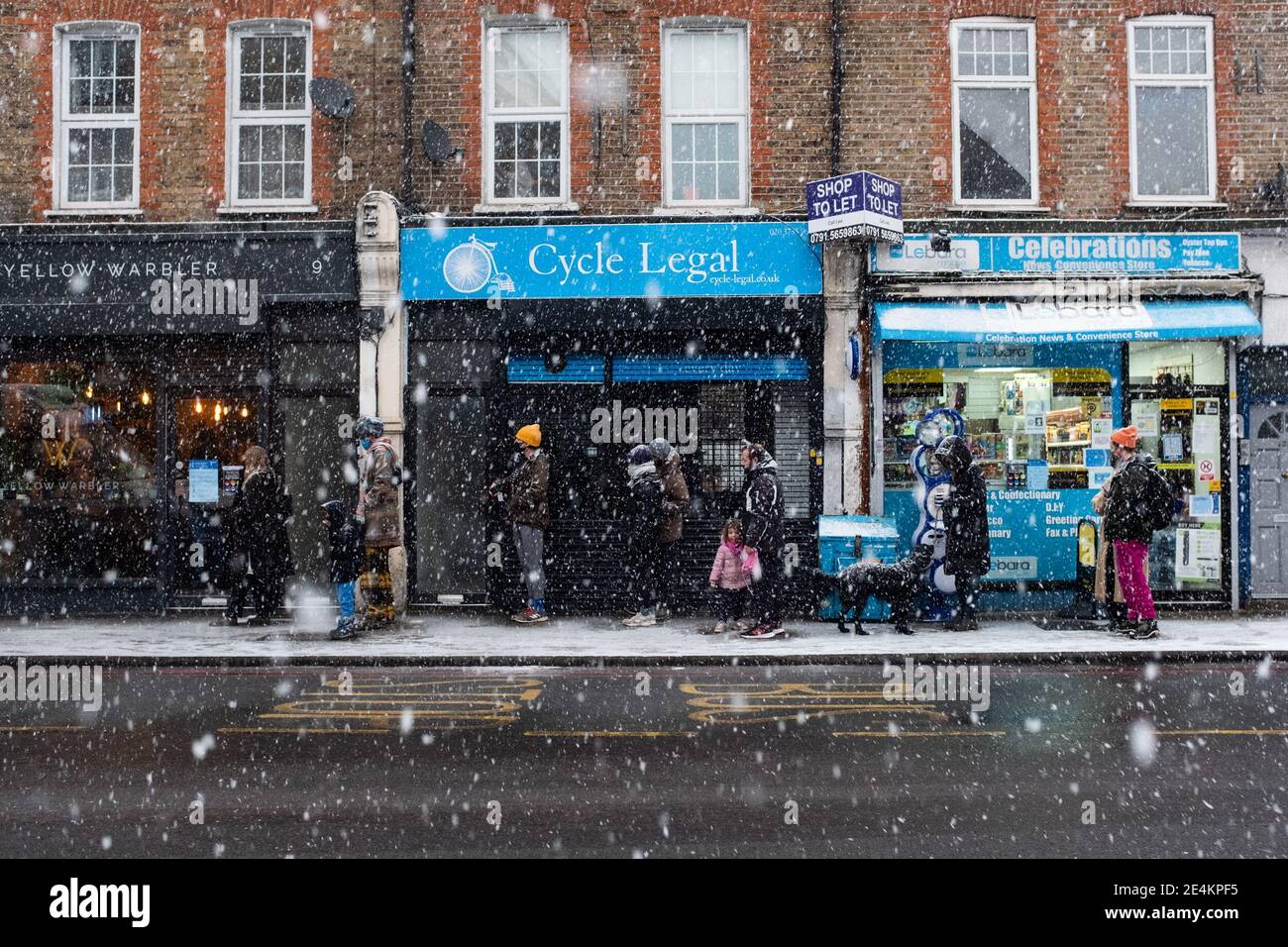 People queue outside a shop as snow falls in Stoke Newington, London. Picture date: Sunday January 24, 2021. Stock Photo