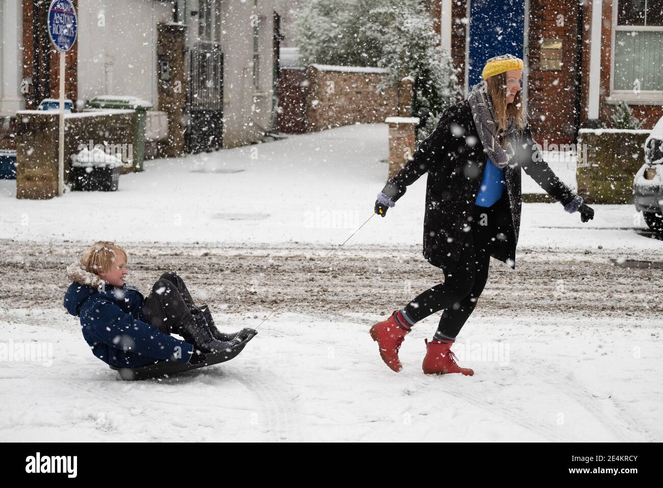 A mother and her son use a sledge to negotiate a snowy road in Kew, southwest London, after swathes of the UK woke up to snow and ice this morning, with even the capital getting a dusting of white. Picture date: Sunday January 24, 2021. Stock Photo
