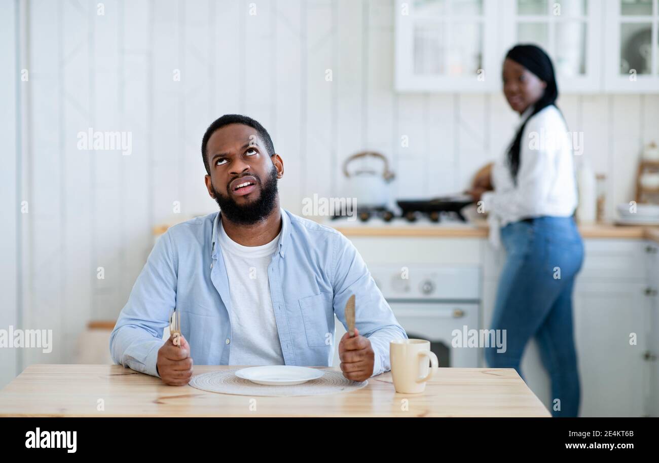 Impatient hungry black husband waiting for dinner with empty plate, looking bored Stock Photo