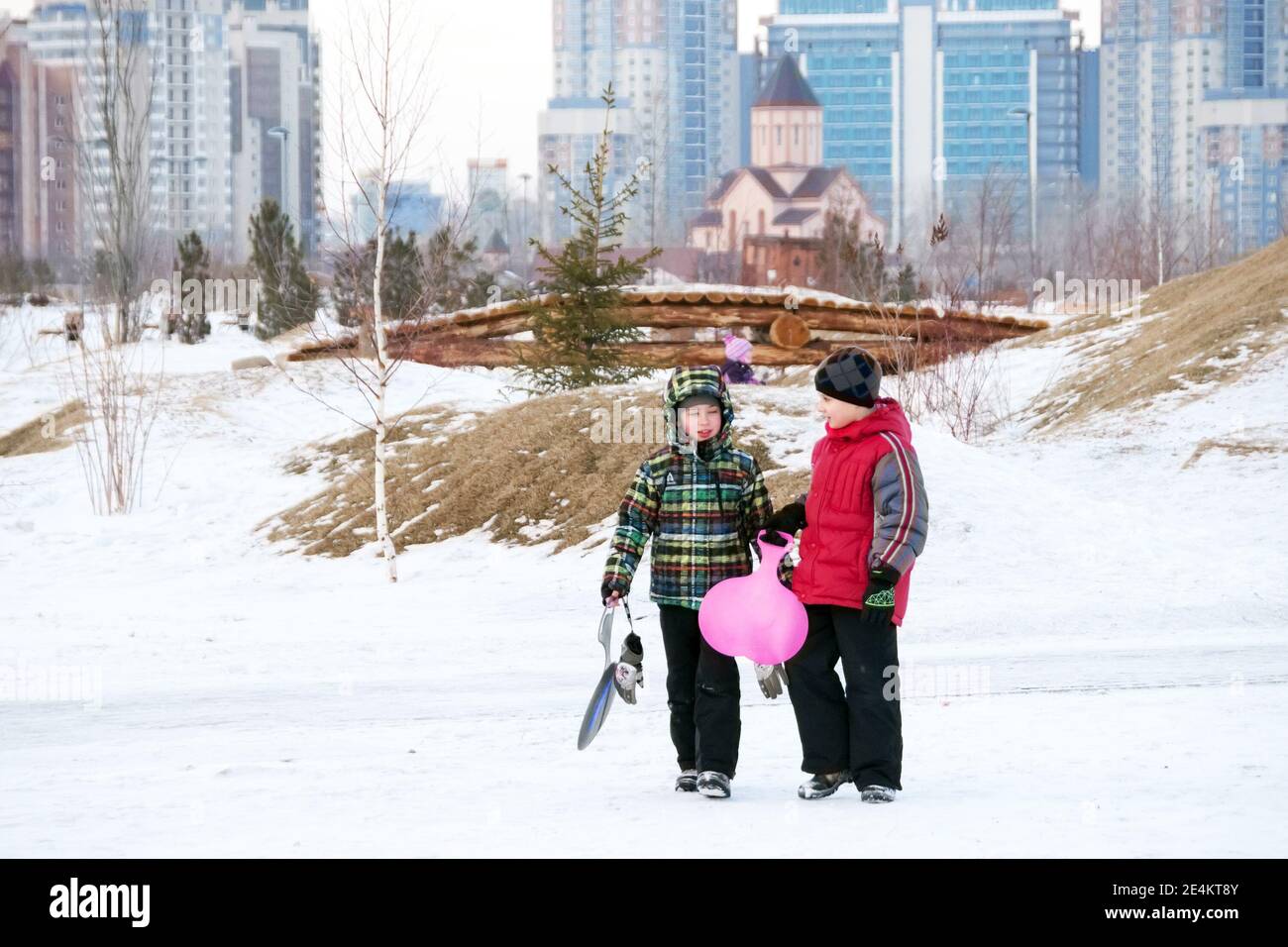 Two friends gathered to ride down the ice slide and walk along the snow-covered park against the backdrop of residential buildings and an Armenian chu Stock Photo