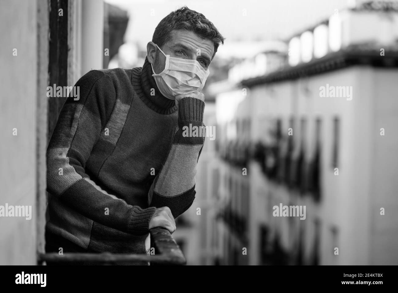 coronavirus dramatic mess - stay home quarantine portrait of attractive man in face mask sad and depressed at home balcony during covid19 lockdown fee Stock Photo