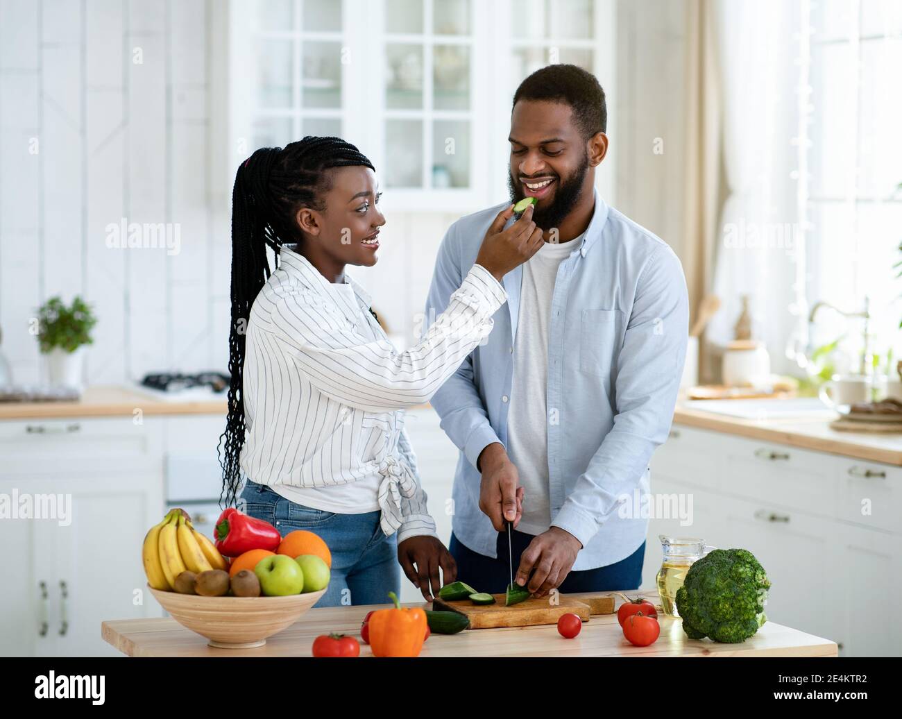 Loving black woman feeding her husband while they cooking together at