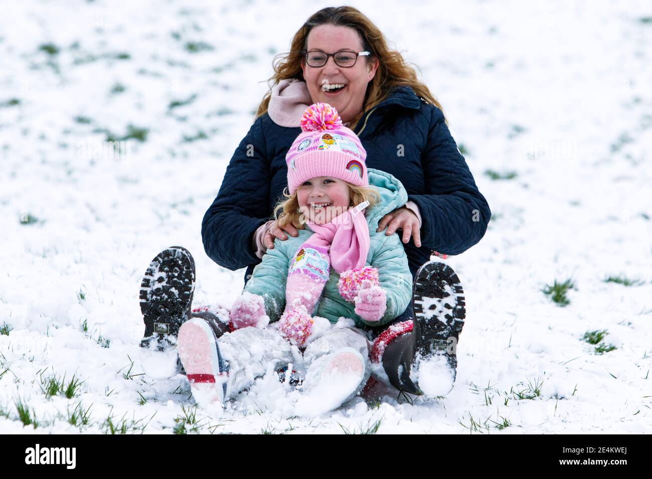 Chippenham, Wiltshire, UK. 24th January, 2021. As Chippenham residents wake up to their first snow of the year, a woman and a child are pictured in a local park in Chippenham as they slide down a hill on a sledge. Credit: Lynchpics/Alamy Live News Stock Photo