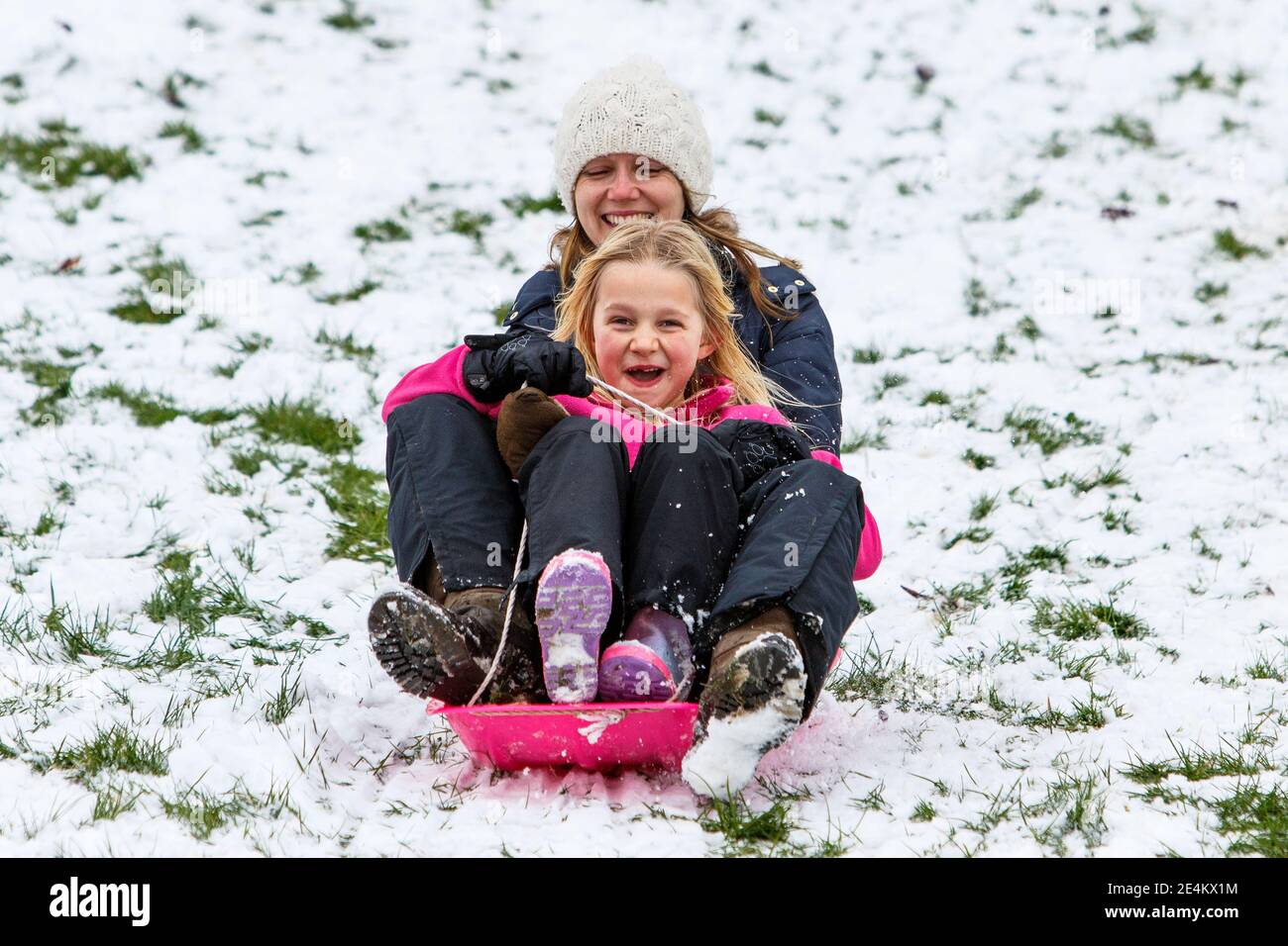 Chippenham, Wiltshire, UK. 24th January, 2021. As Chippenham residents wake up to their first snow of the year, a woman and a child are pictured in a local park in Chippenham as they slide down a hill on a sledge. Credit: Lynchpics/Alamy Live News Stock Photo