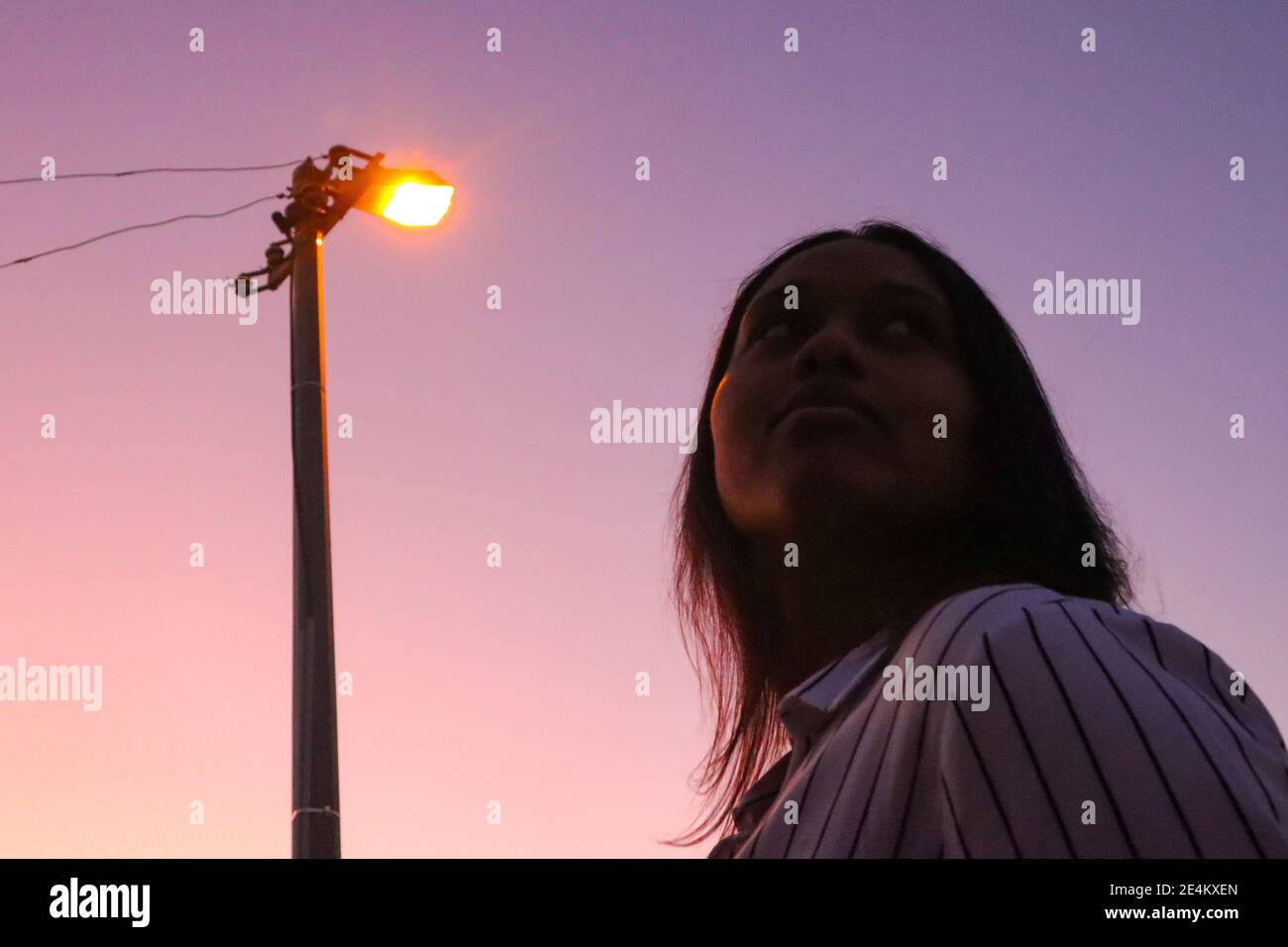 Cape Town, South Africa - 20-02-2020 Creative and hazy purple sunset and street lamp. Stylish young woman silhouetted in foreground. Stock Photo