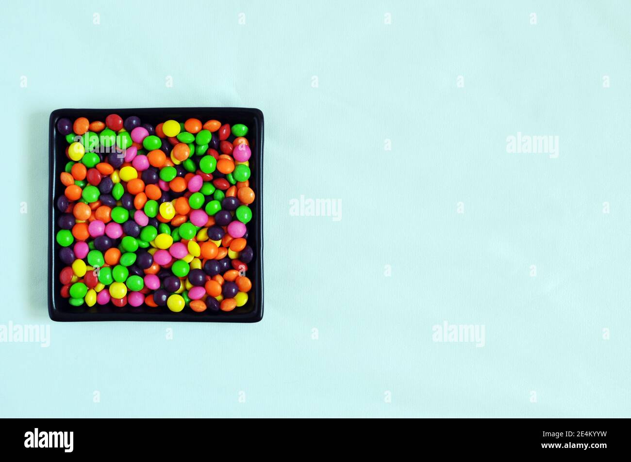 Minimalist black plate filled with little colorful candies on light blue background, copy space, top view Stock Photo