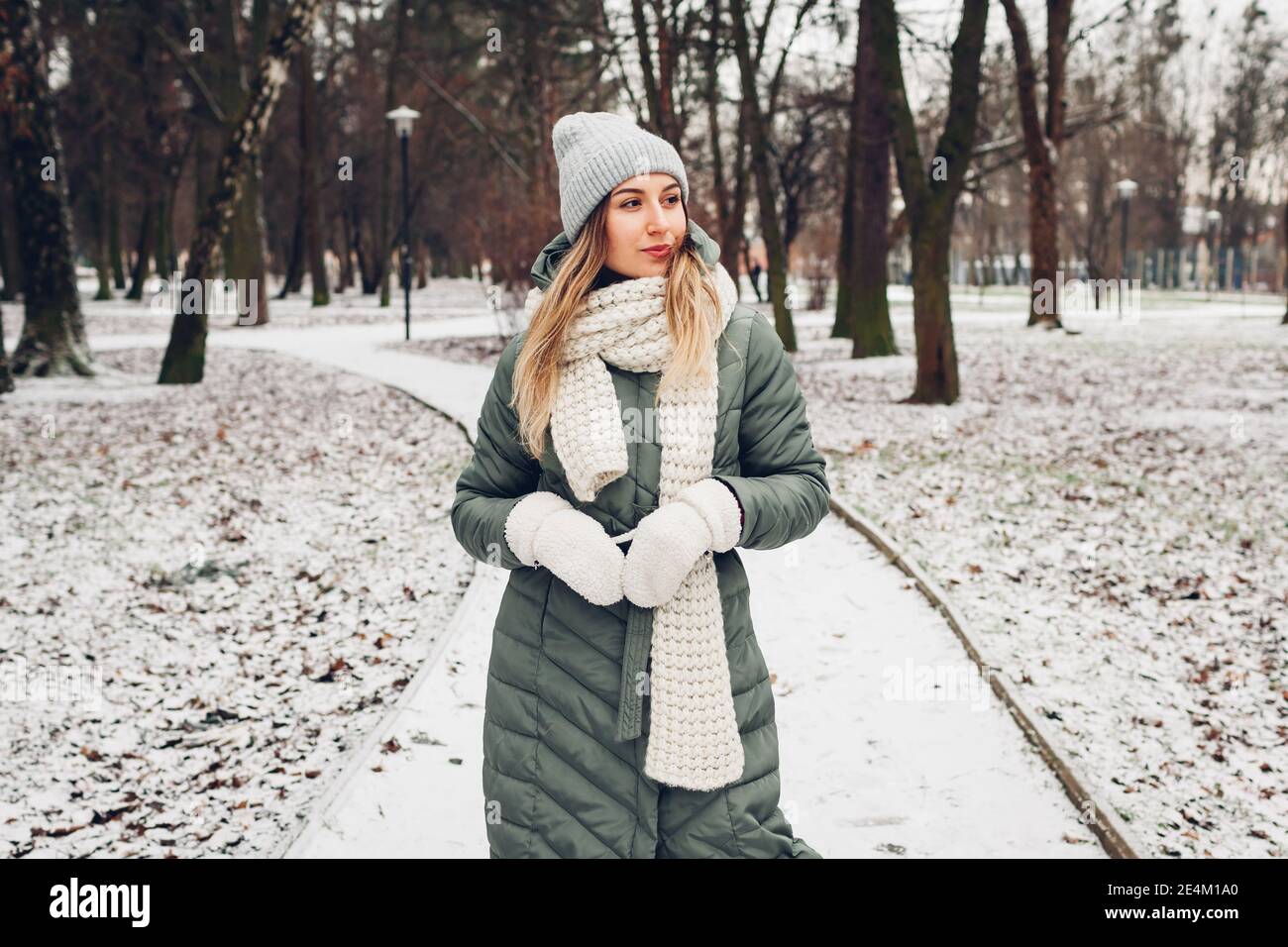 Winter fashion. Portrait of young woman wearing long green coat with scarf,  hat, mittens in snowy park. Modern clothes Stock Photo - Alamy