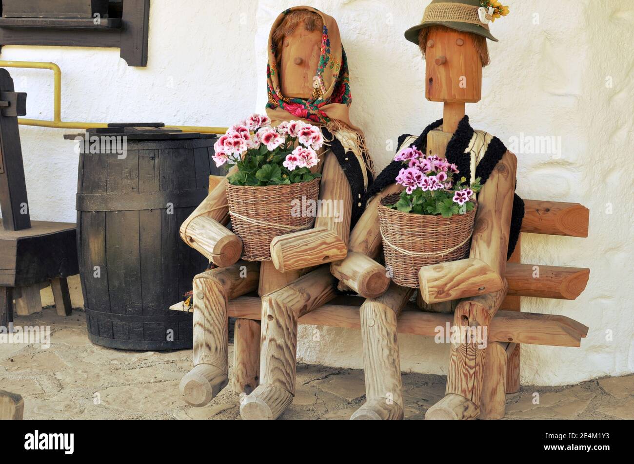 Wooden decorative toys sitting on a bench in front of a house with flower pot in hands. Filter applied. Stock Photo