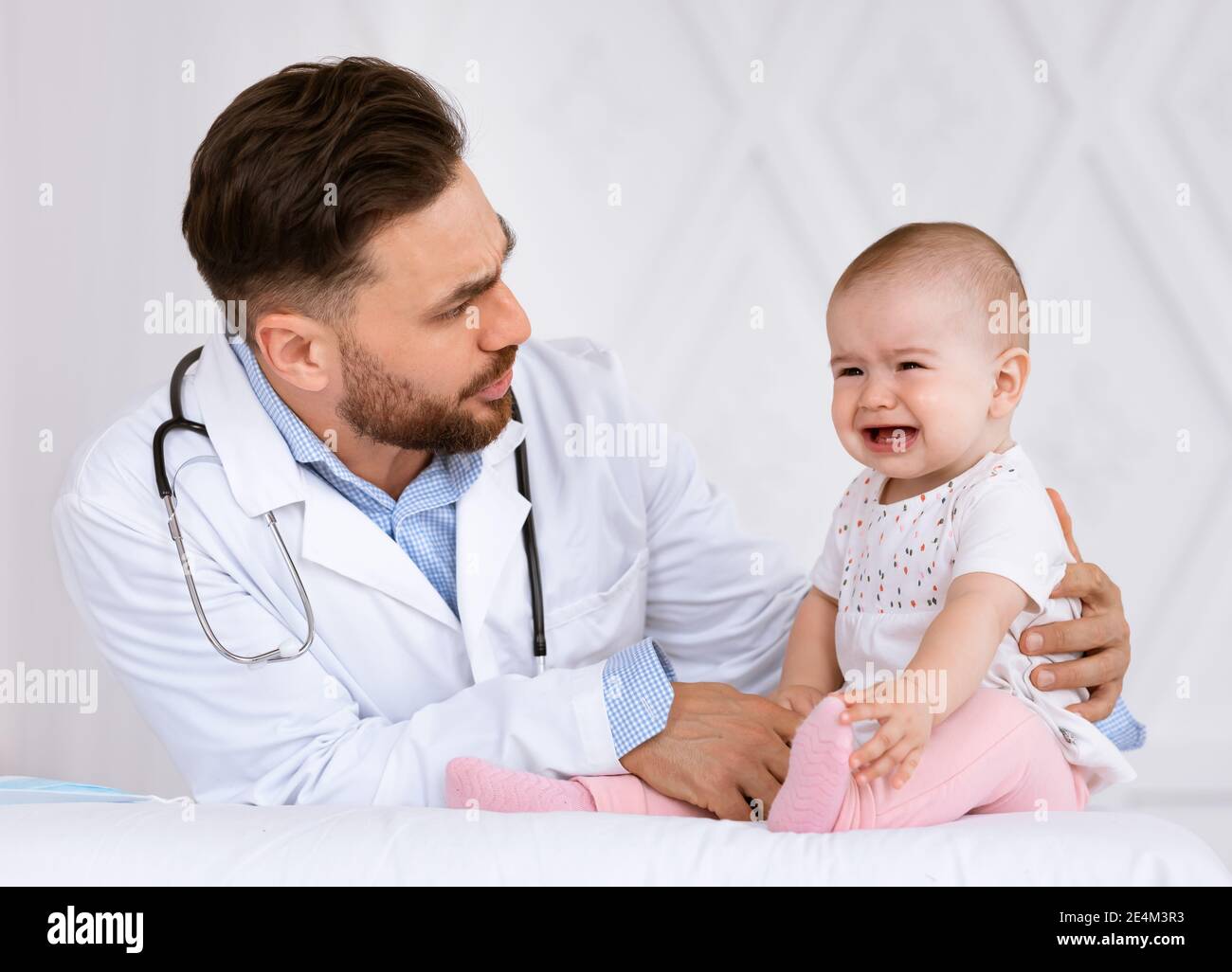 Baby Crying On Medical Checkup With Doctor Sitting In Clinic Stock Photo