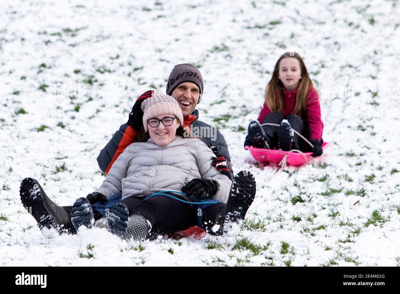 Chippenham, Wiltshire, UK. 24th January, 2021. As Chippenham residents wake up to their first snow of the year, a couple and a child are pictured in a local park in Chippenham as they slide down a hill on sledges. Credit: Lynchpics/Alamy Live News Stock Photo