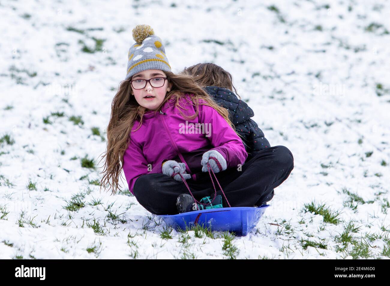Chippenham, Wiltshire, UK. 24th January, 2021. As Chippenham residents wake up to their first snow of the year,two children are pictured in a local park in Chippenham as they slide down a hill on a sledge. Credit: Lynchpics/Alamy Live News Stock Photo