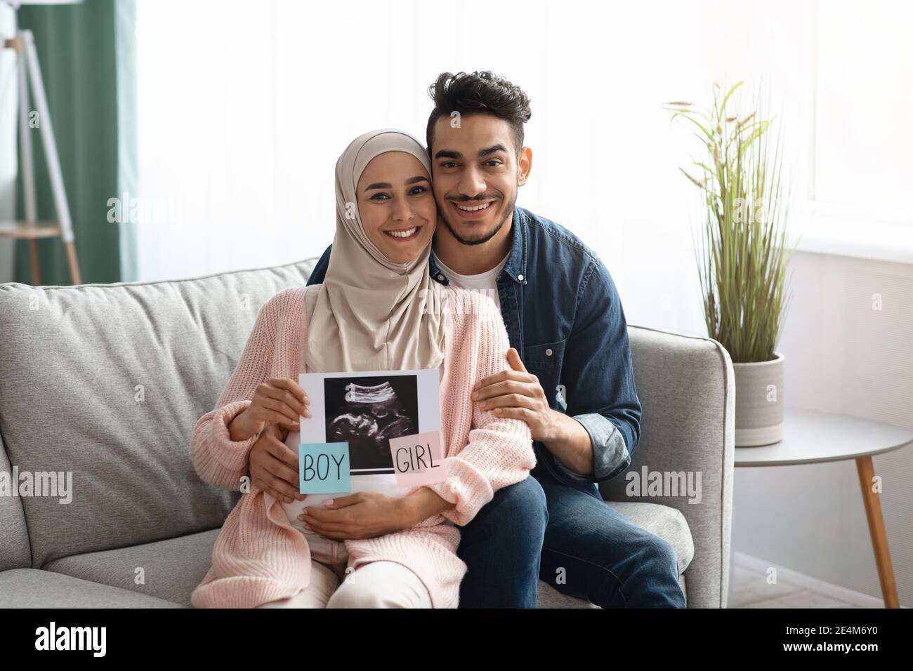 Gender Reveal. Happy pregnant muslim couple holding baby ultrasound photo at home Stock Photo