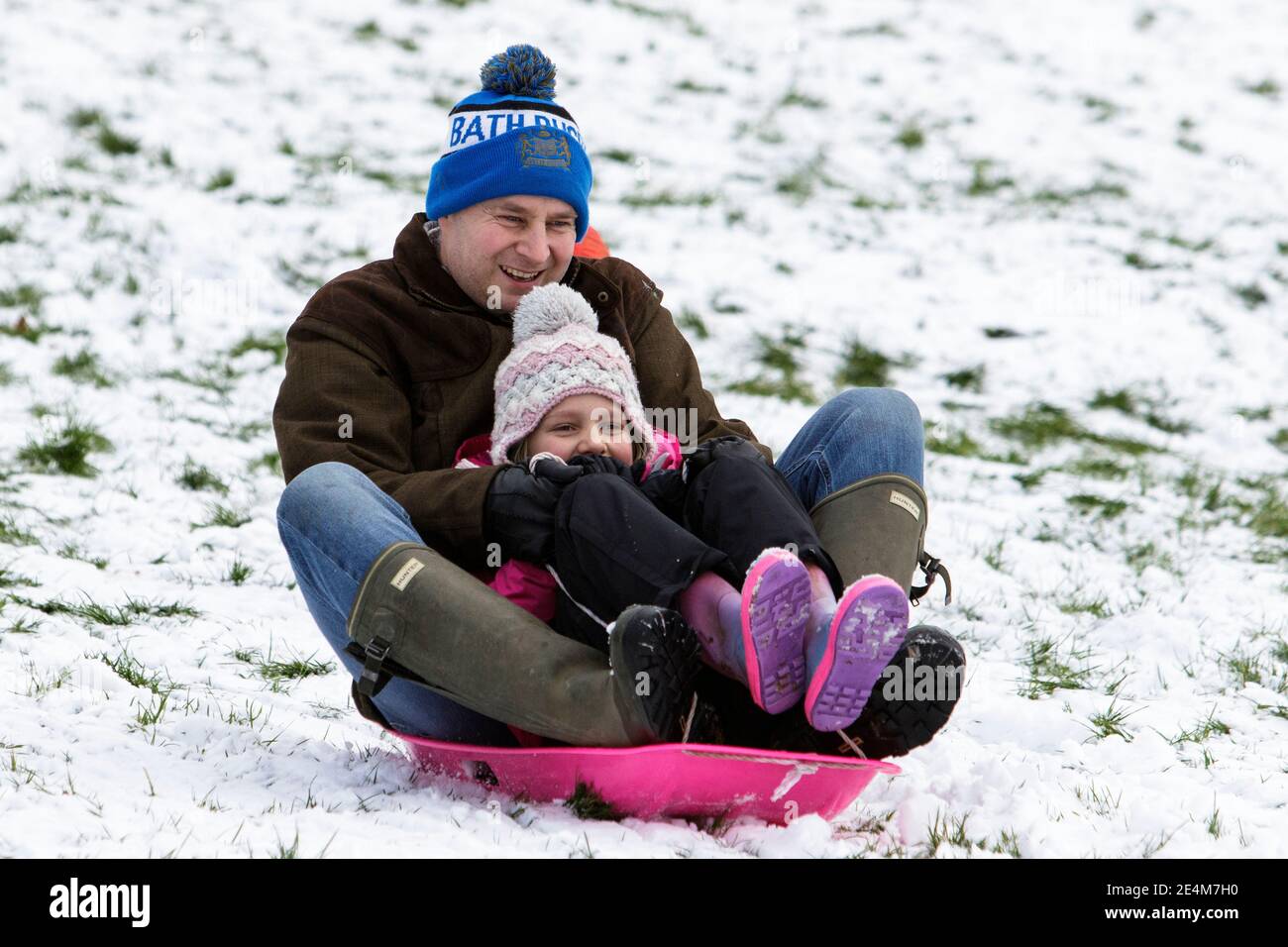 Chippenham, Wiltshire, UK. 24th January, 2021. As Chippenham residents wake up to their first snow of the year, a man and a young child are pictured in a local park in Chippenham as they slide down a hill on a sledge. Credit: Lynchpics/Alamy Live News Stock Photo