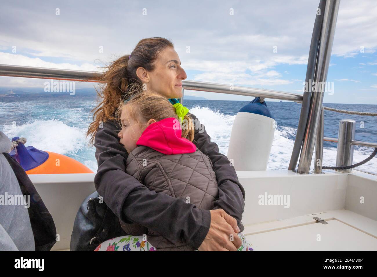 mother hugging her daughter, four years old blonde girl with pigtail, sitting on the stern of motorboat sailing from Tarifa (Cadiz, Andalusia, Spain) Stock Photo