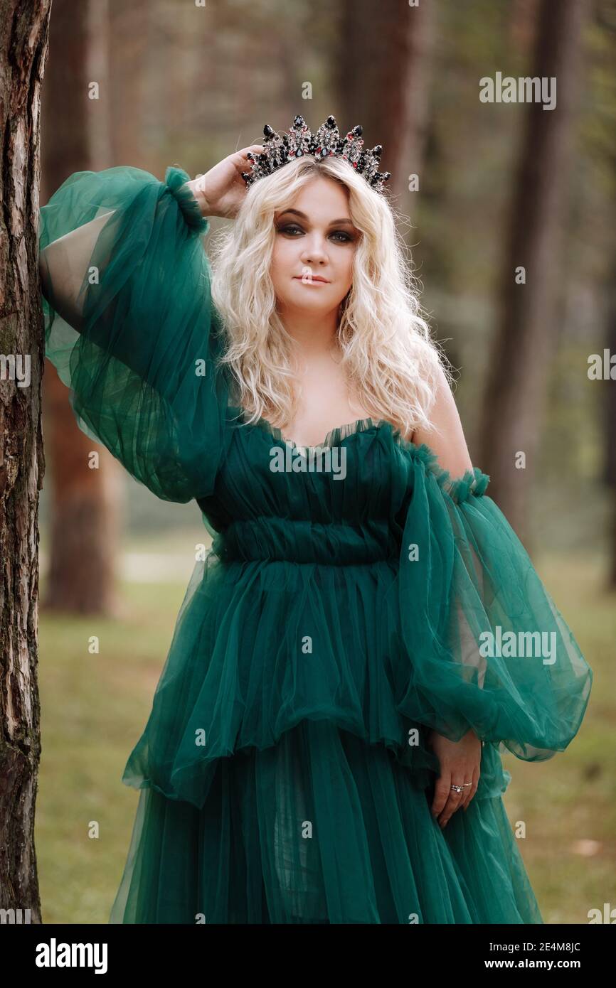 young beautiful blonde hair woman queen. Princess walks. autumn green  forest mystic. Vintage medieval shiny crown. Long evening green dress.  magic fan Stock Photo - Alamy