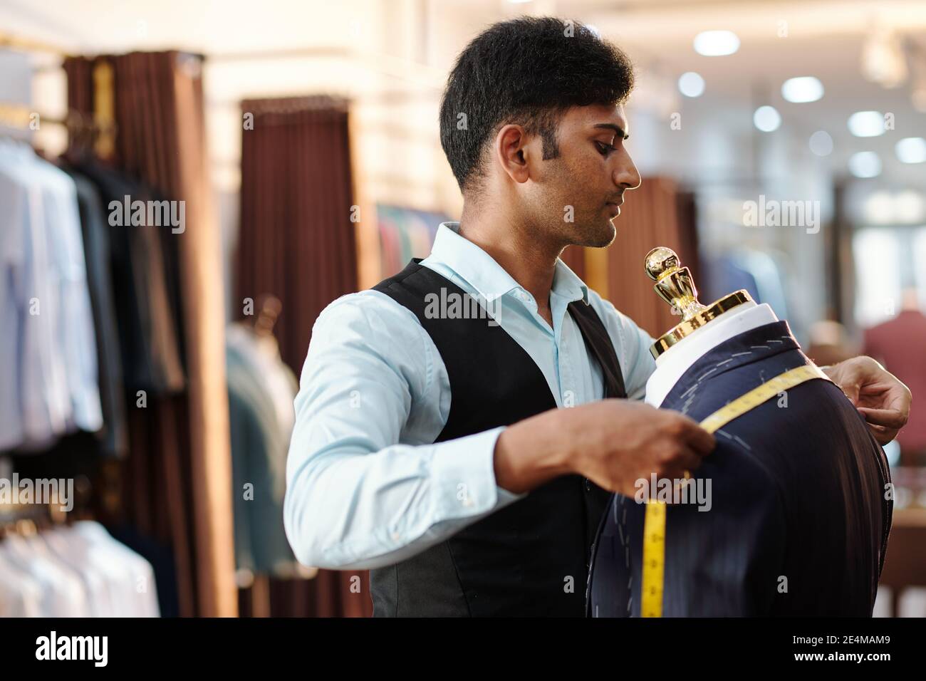 Concentrated young Indian tailor measuring bespoke jacket shoulders with tape measure Stock Photo
