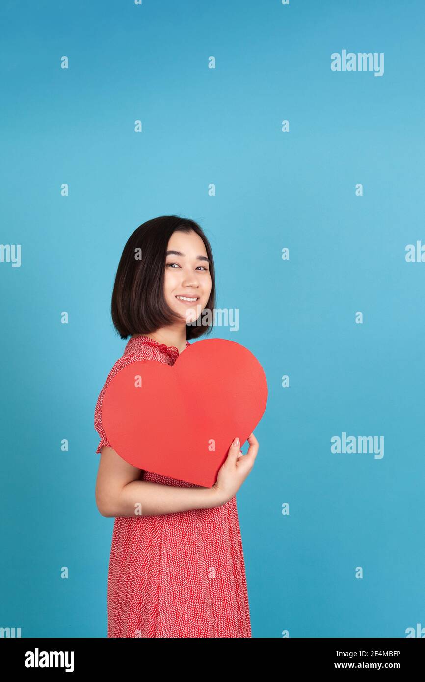 joyful, cheerful young asian woman in red dress holding big red paper ...
