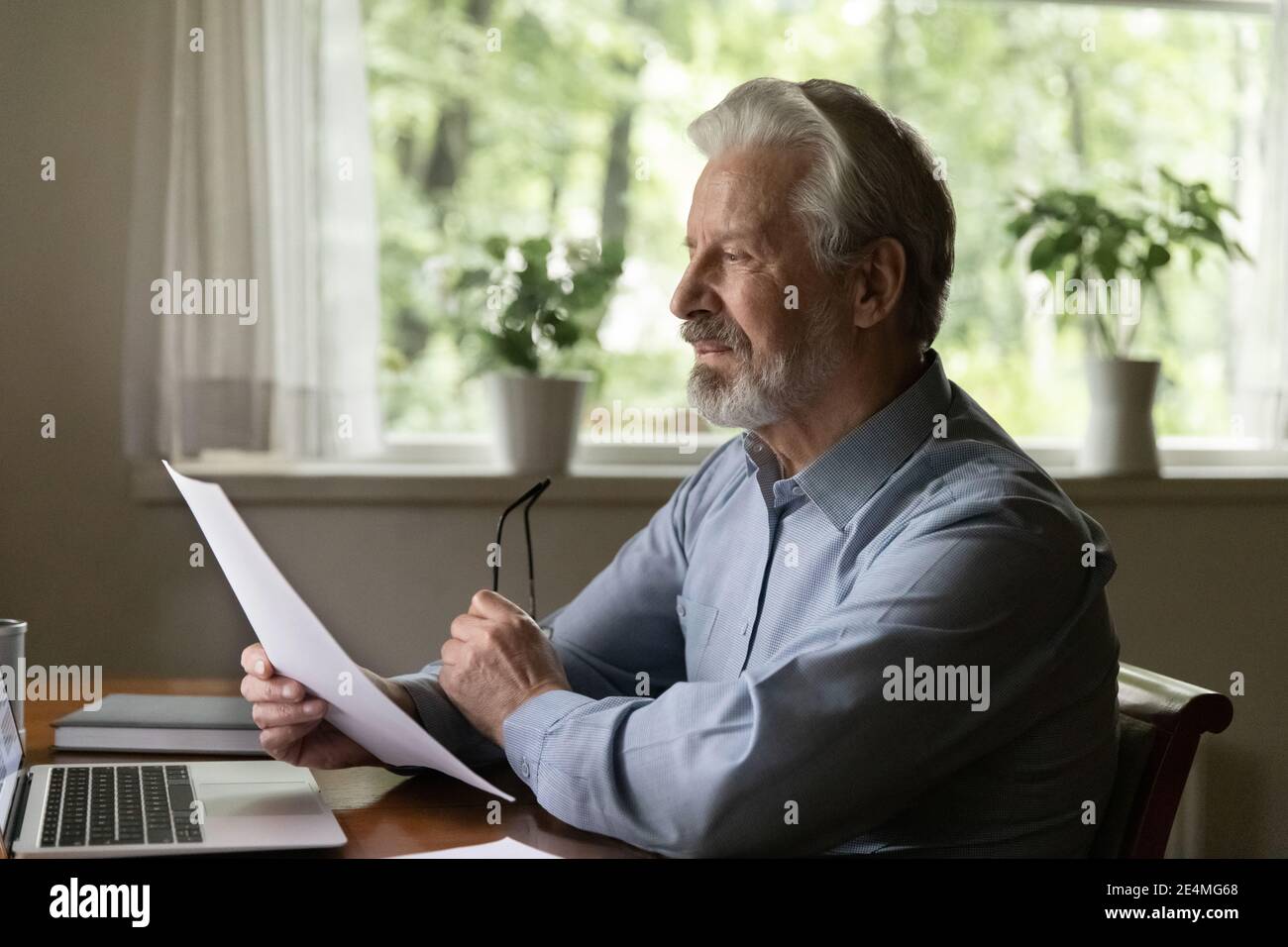 Focused elderly man reading letter, checking documents, working with correspondence Stock Photo