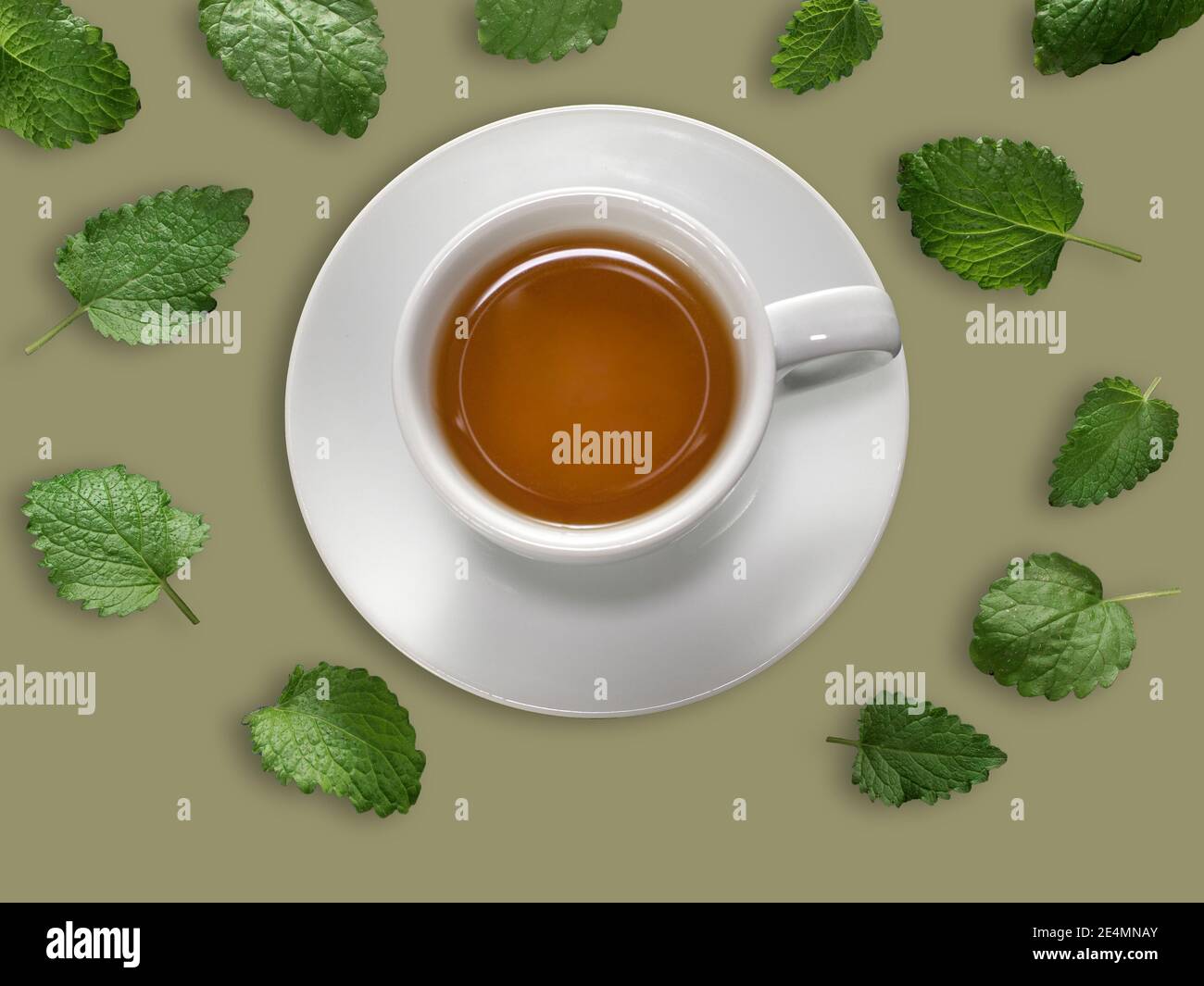 White cup of mint tea with meant leaves on green background. Overhead shot. Stock Photo