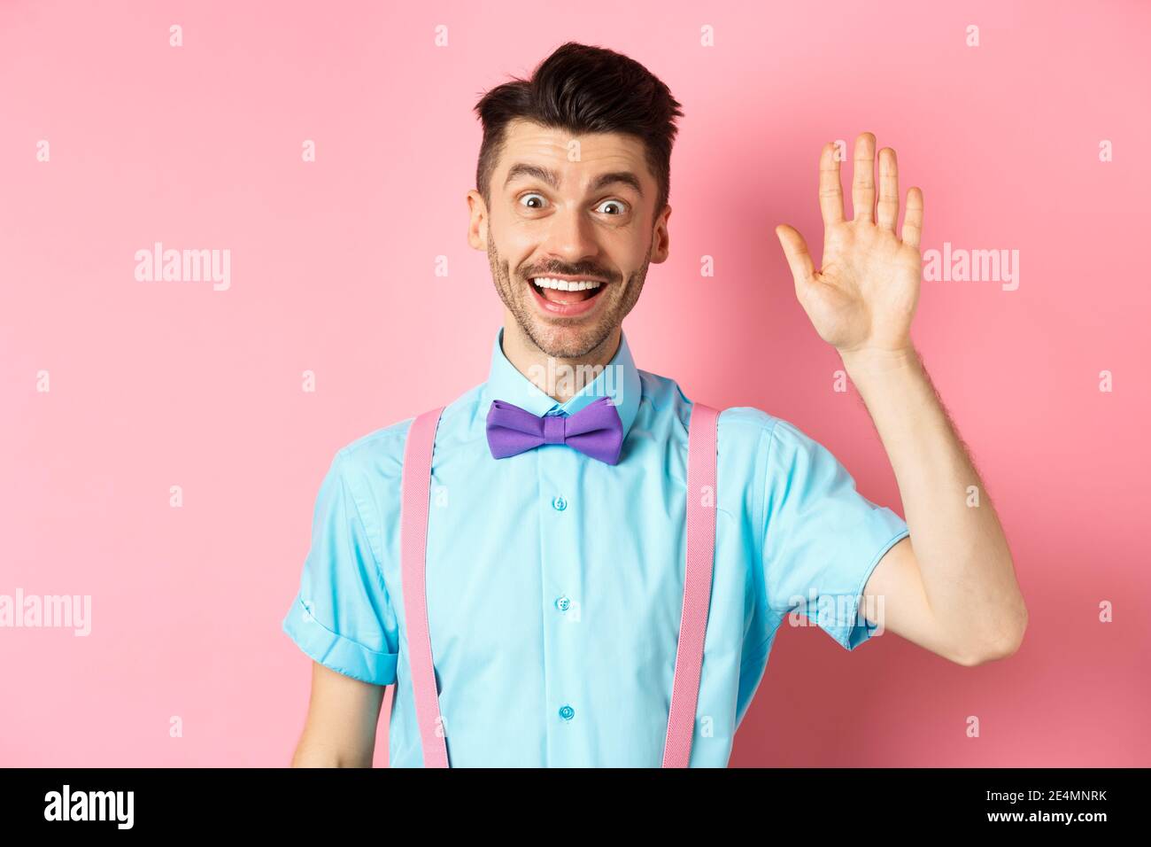 Friendly smiling man in funny bow-tie saying hello, waving hand to greet  you, make hi gesture and looking happy yo see you, standing over pink Stock  Photo - Alamy