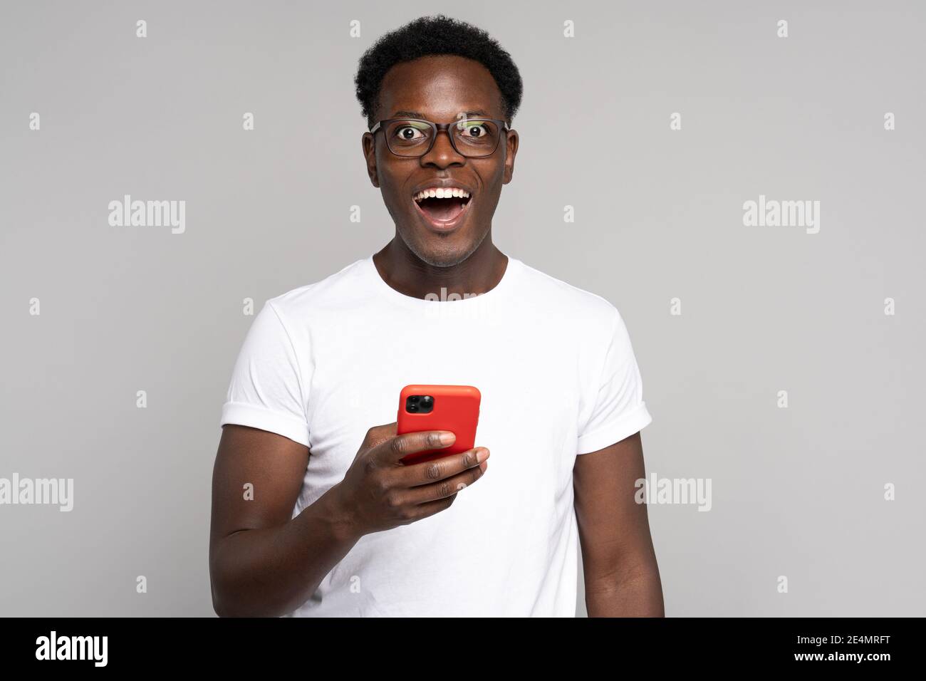 Happy African millennial man in glasses wear white t-shirt, holding mobile phone, isolated on studio Stock Photo