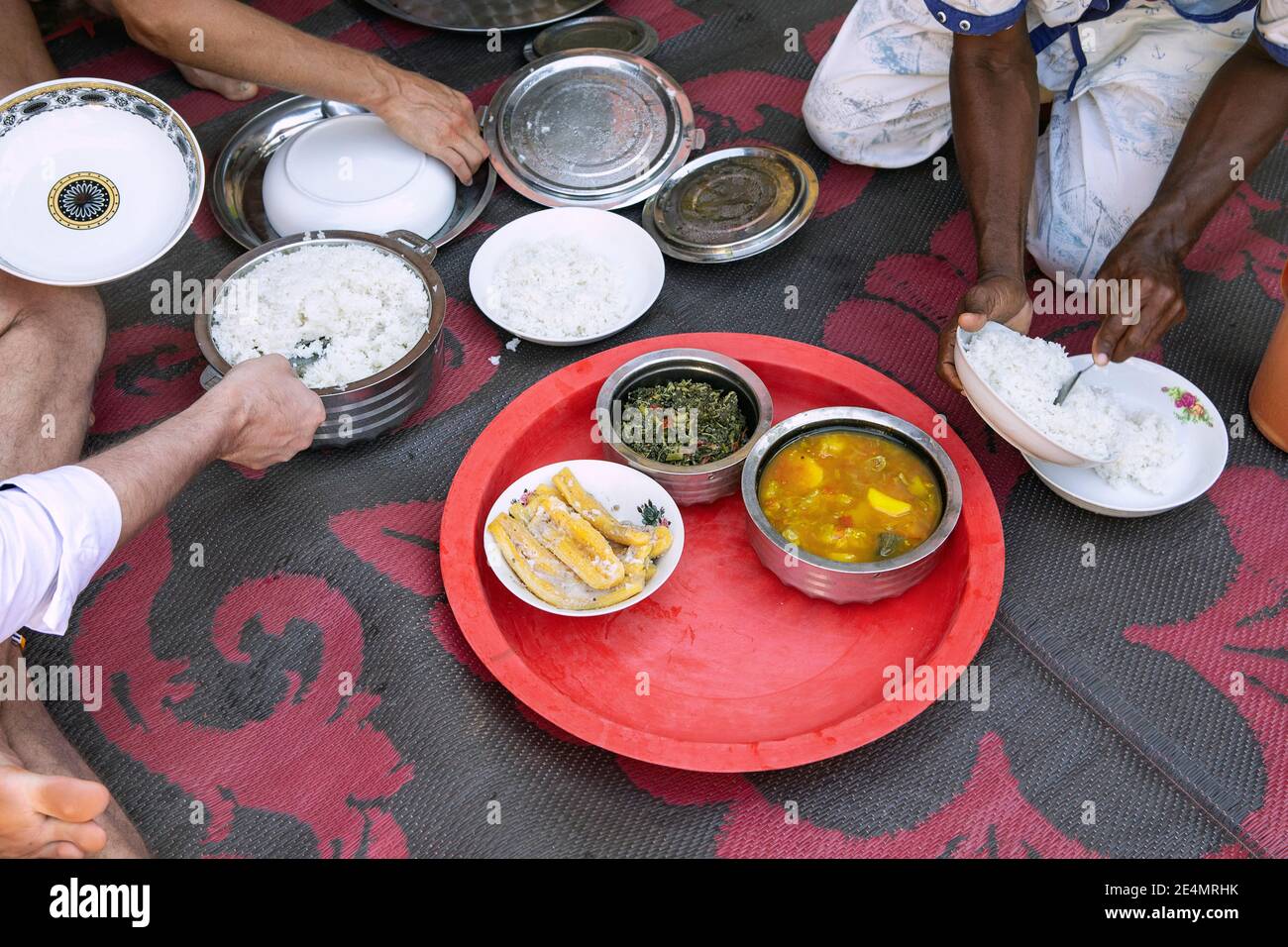 African food on the ground in african village house. People put food on the plate, visible hands. Homemade dishes ready to eat, view from above. Stock Photo