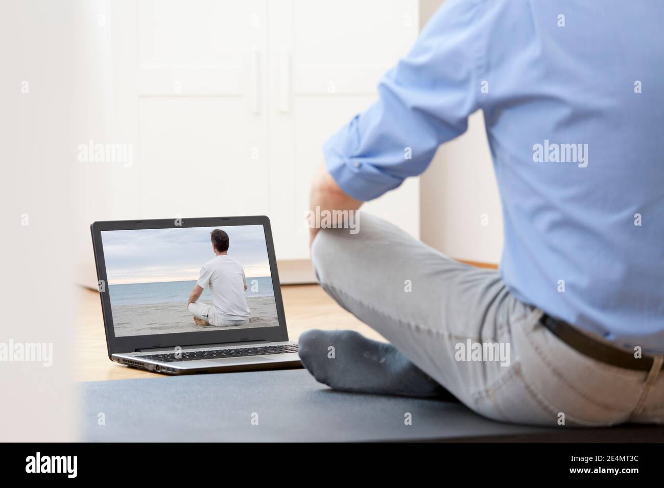 Businessman doing yoga or meditation exercise in front of laptop with man doing yoga on a beach - focus on the screen Stock Photo