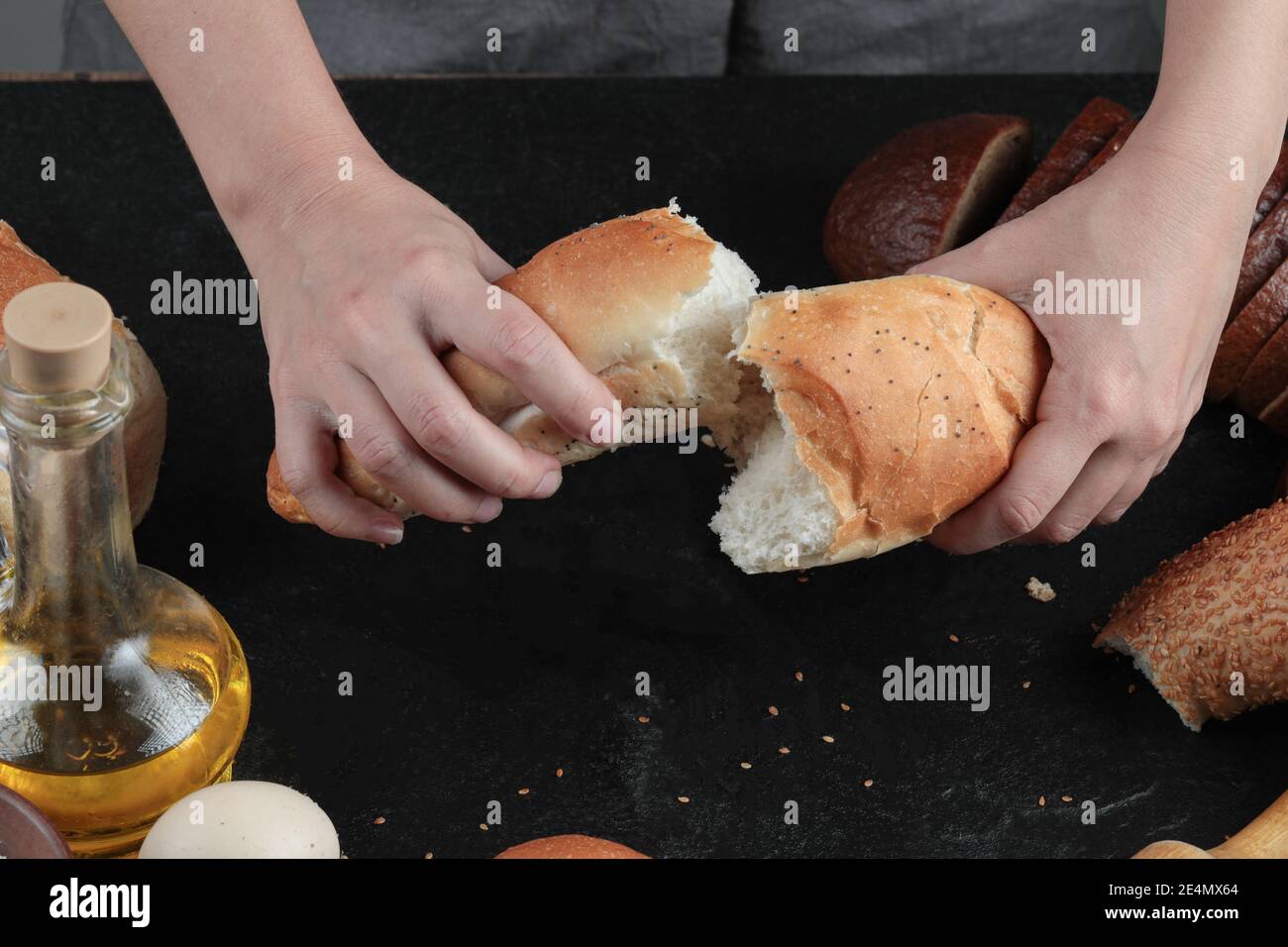 Woman cut bread into half on dark table with eggs and glass of oil Stock Photo