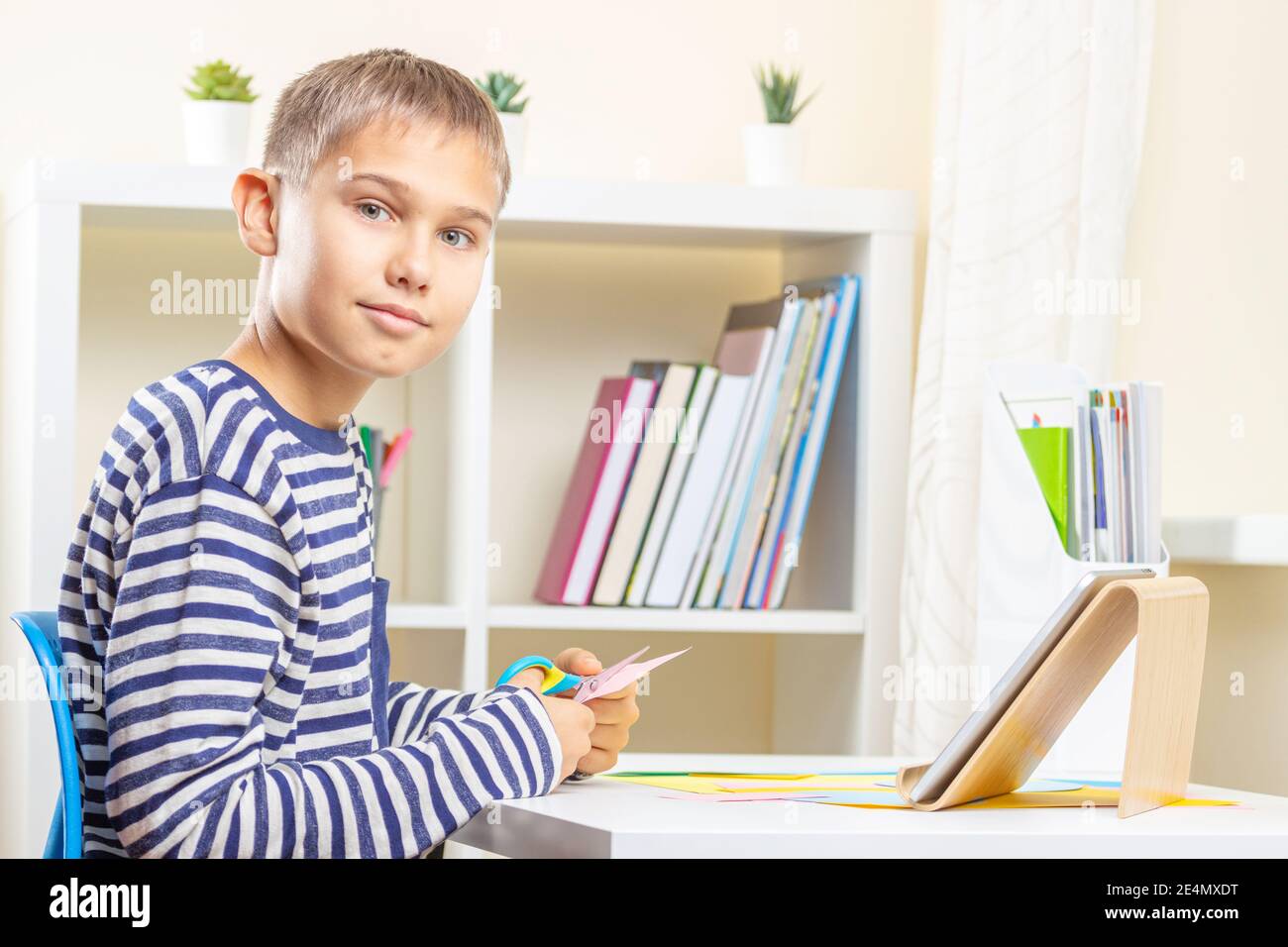 Boy Using Paper Teenage boy cutting colored paper with scissors. Kid looking video ...
