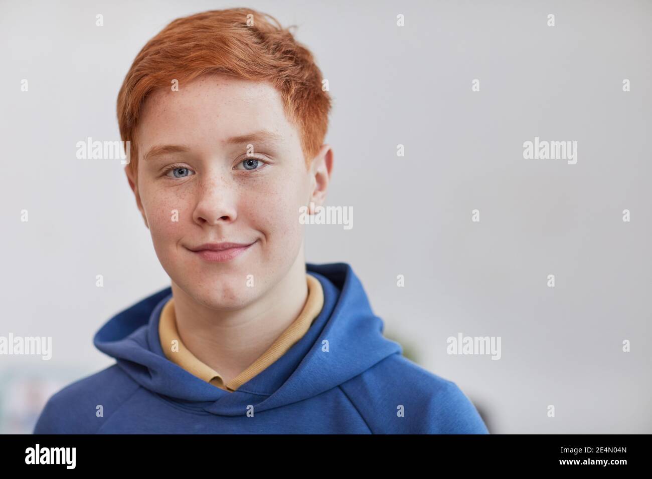 Head and shoulders portrait of freckled red haired boy looking at camera and smiling while standing against white background, copy space Stock Photo