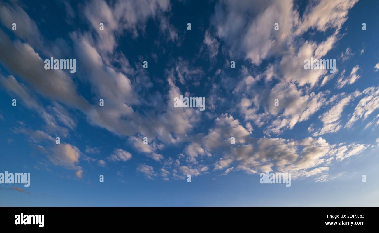 White fluffy clouds in deep blue azure summer sunset sky with sunlight ...