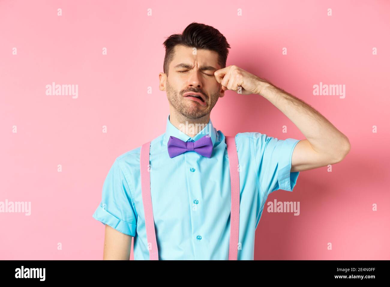 Image of heartbroken guy crying and wiping tear off face, sobbing and feeling sad or lonely, standing upset on pink background Stock Photo