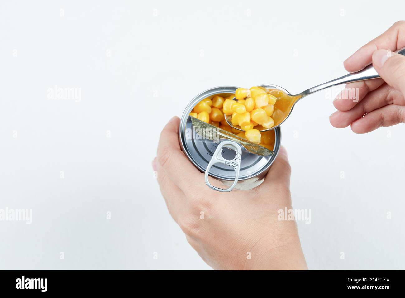 Hand taking a spoon of boiled sweet corn from a tin can on a white background Stock Photo