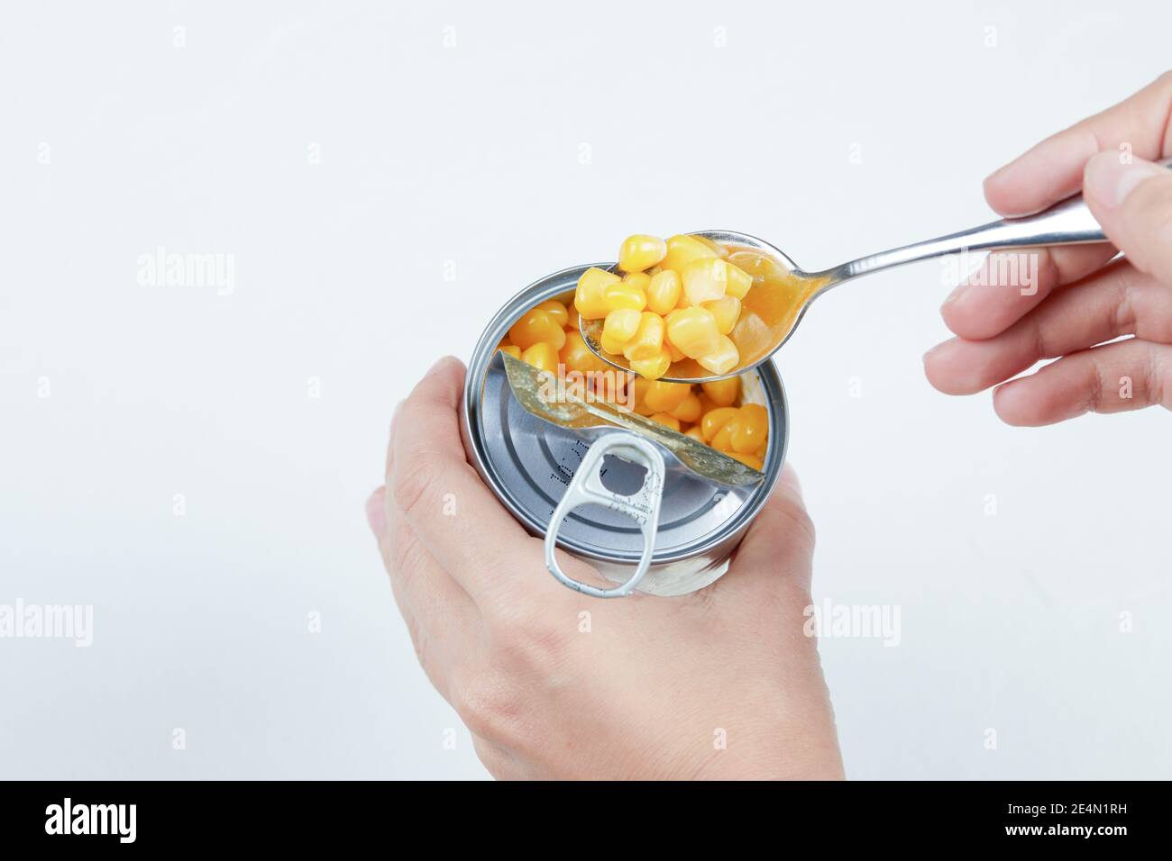 Hand taking a spoon of boiled sweet corn from a tin can on a white background Stock Photo