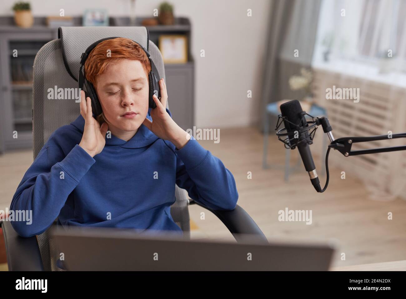 Portrait of red haired teenage boy wearing headphones and enjoying music with eyes closed while relaxing or recording podcast, copy space Stock Photo